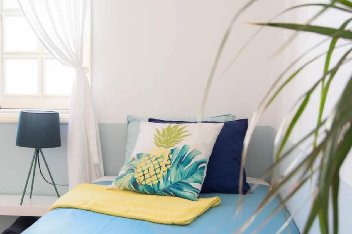 Una cama con una colcha azul, un plaid amarillo y una almohada con motivos de piña.