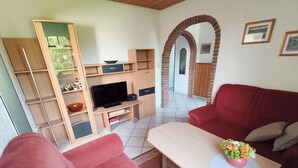 A living room with a red sofa, a wooden coffee table, a TV, and a bookshelf. - Vacation apartment on the North Sea - Holtgast (East Frisia) (Holtgast)