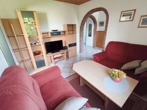 Un salon avec un canapé rouge, une table basse en bois, un téléviseur et une bibliothèque.