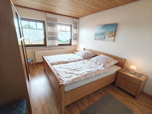 Une chambre à coucher avec un lit en bois, deux tables de chevet, un radiateur, une fenêtre avec des stores et un tableau au mur.