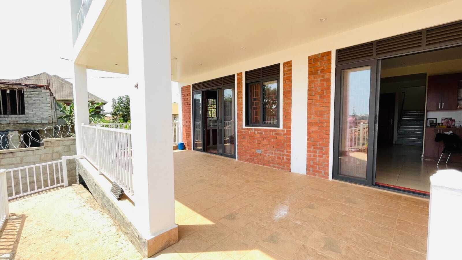 Un espacio al aire libre techado con piso de baldosas, barandal blanco y pared de ladrillo.
