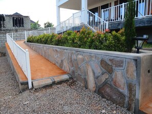 Een stenen steunmuur met een witte balustrade, een grindpad en een gebouw met balkon.