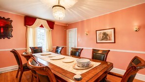 Ein Esszimmer mit einem langen Holztisch, sechs Stühlen, einer Pendelleuchte und einem gerahmten Bild an der Wand.