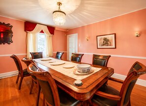 Ein Esszimmer mit einem langen Holztisch, sechs Stühlen, einer Pendelleuchte und einem gerahmten Bild an der Wand.