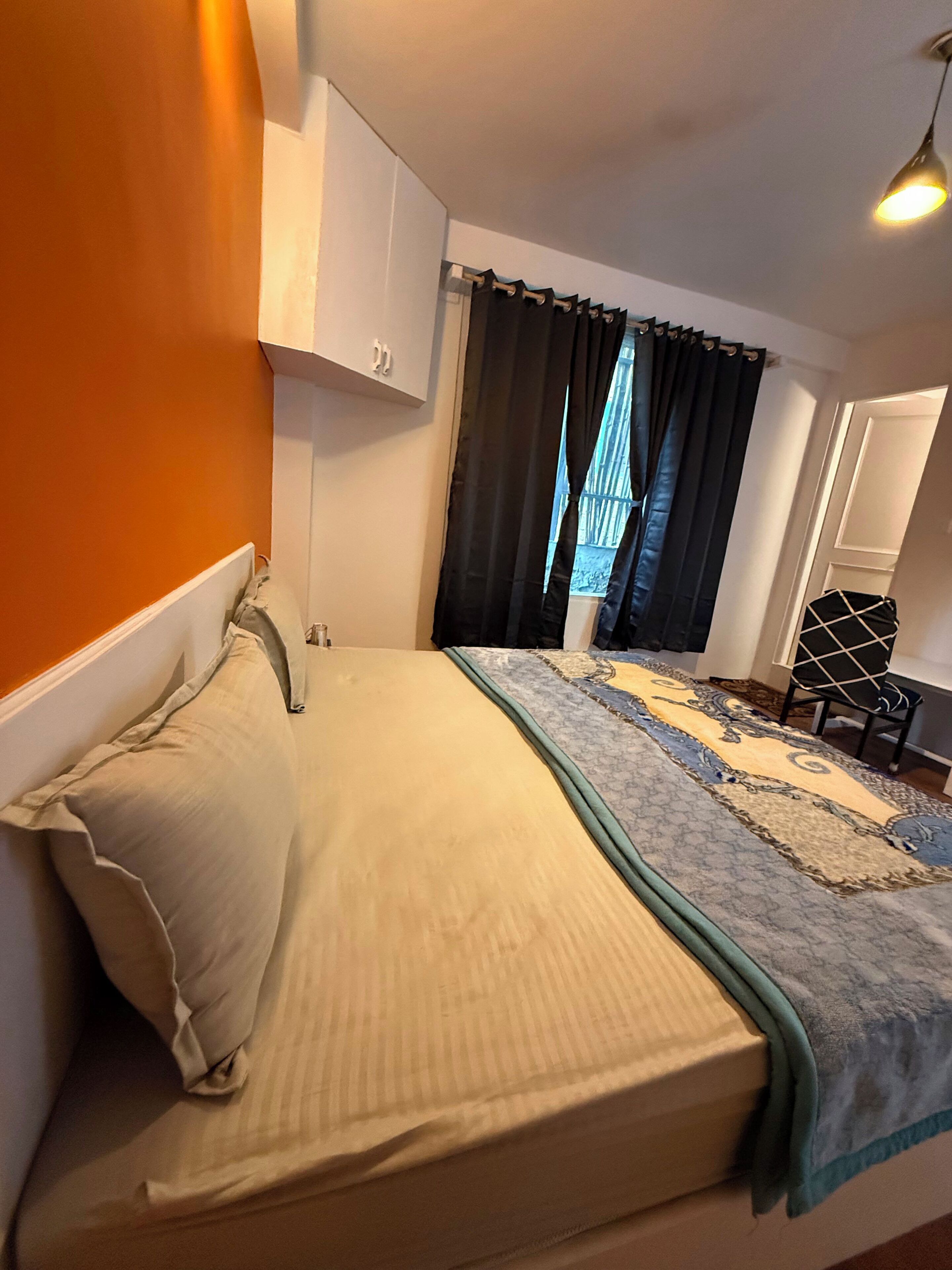 A bedroom with a bed, a window with curtains, a chair, and a wardrobe.