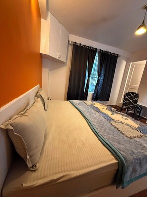 A bedroom with a bed, a window with curtains, a chair, and a wardrobe. - Revivo The Confluenz (Manali)