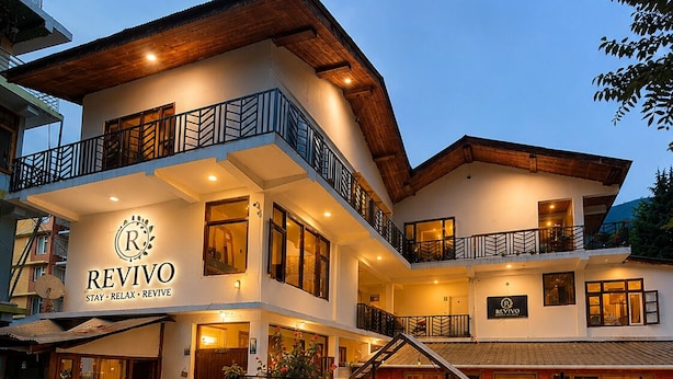 A multi-story hotel with a balcony, a sign reading 'REVIVO,' and a well-lit entrance. - Revivo The Confluenz (Manali)