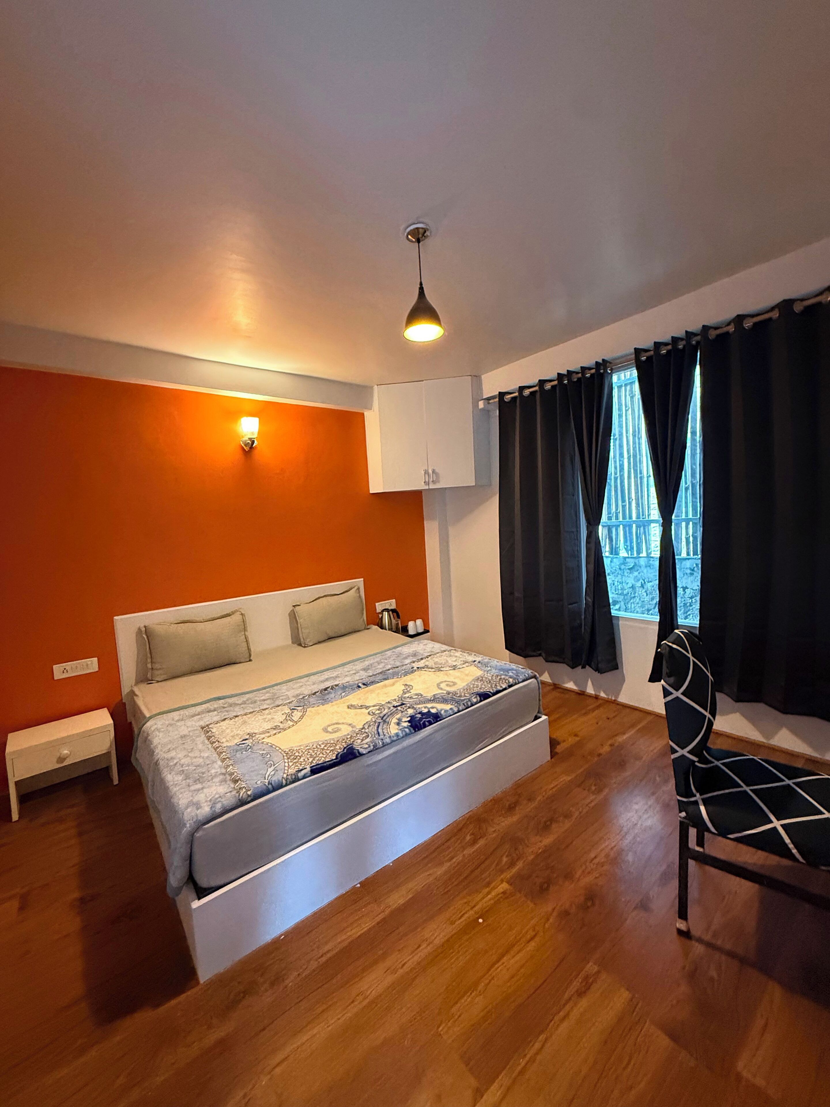 A bedroom with a bed, a chair, a wardrobe, and a window with curtains.