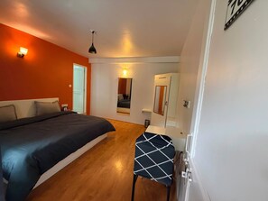 A bedroom with a bed, a small table, a mirror, and a door. - Revivo The Confluenz (Manali)