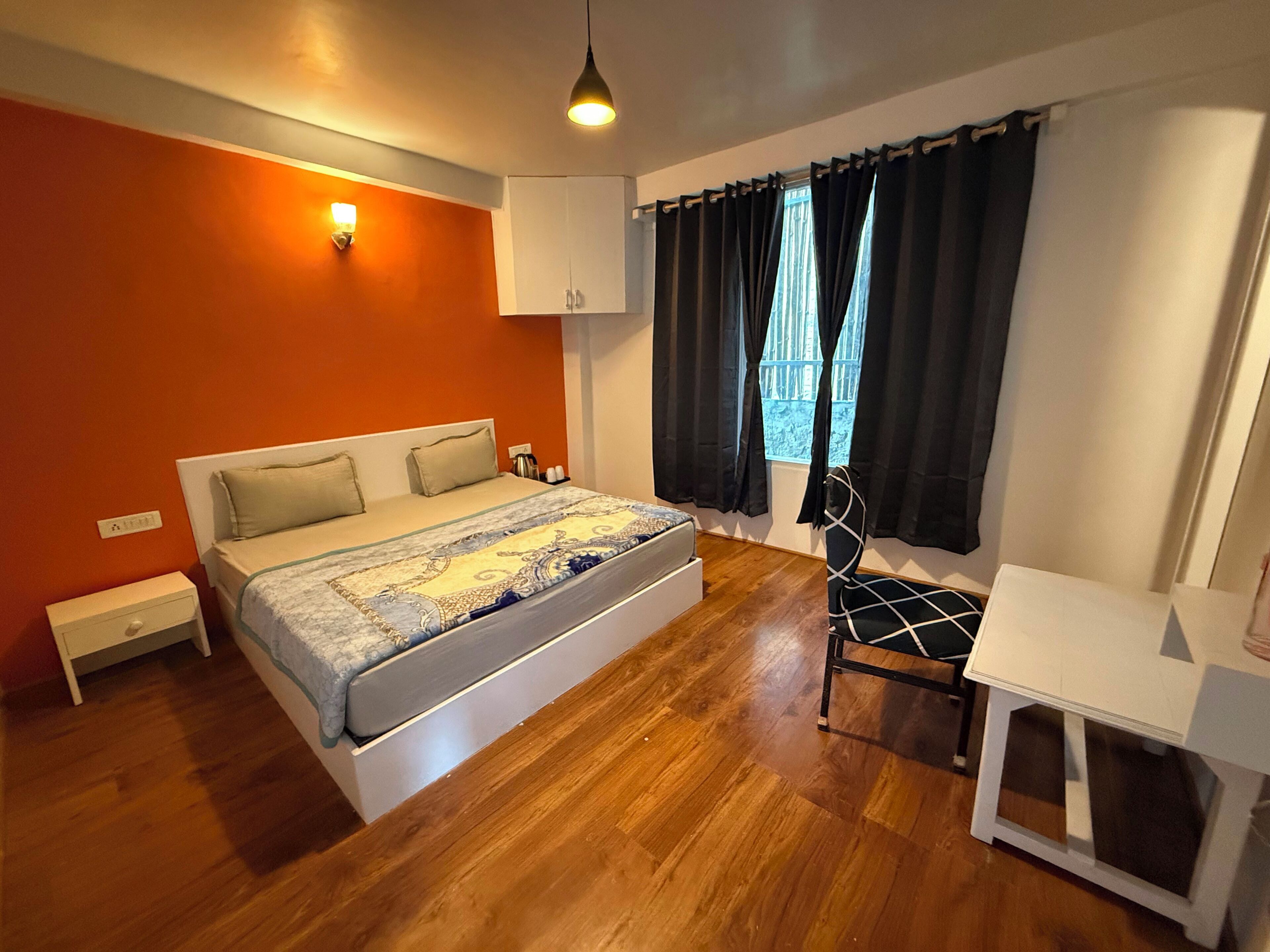 A bedroom with a bed, bedside table, chair, and a window with curtains.