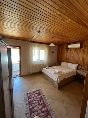 A bedroom with a wooden ceiling, a bed with white linens, a nightstand, a window with curtains, and a radiator. - kabile motel (Çanakkale/Ayvacık)