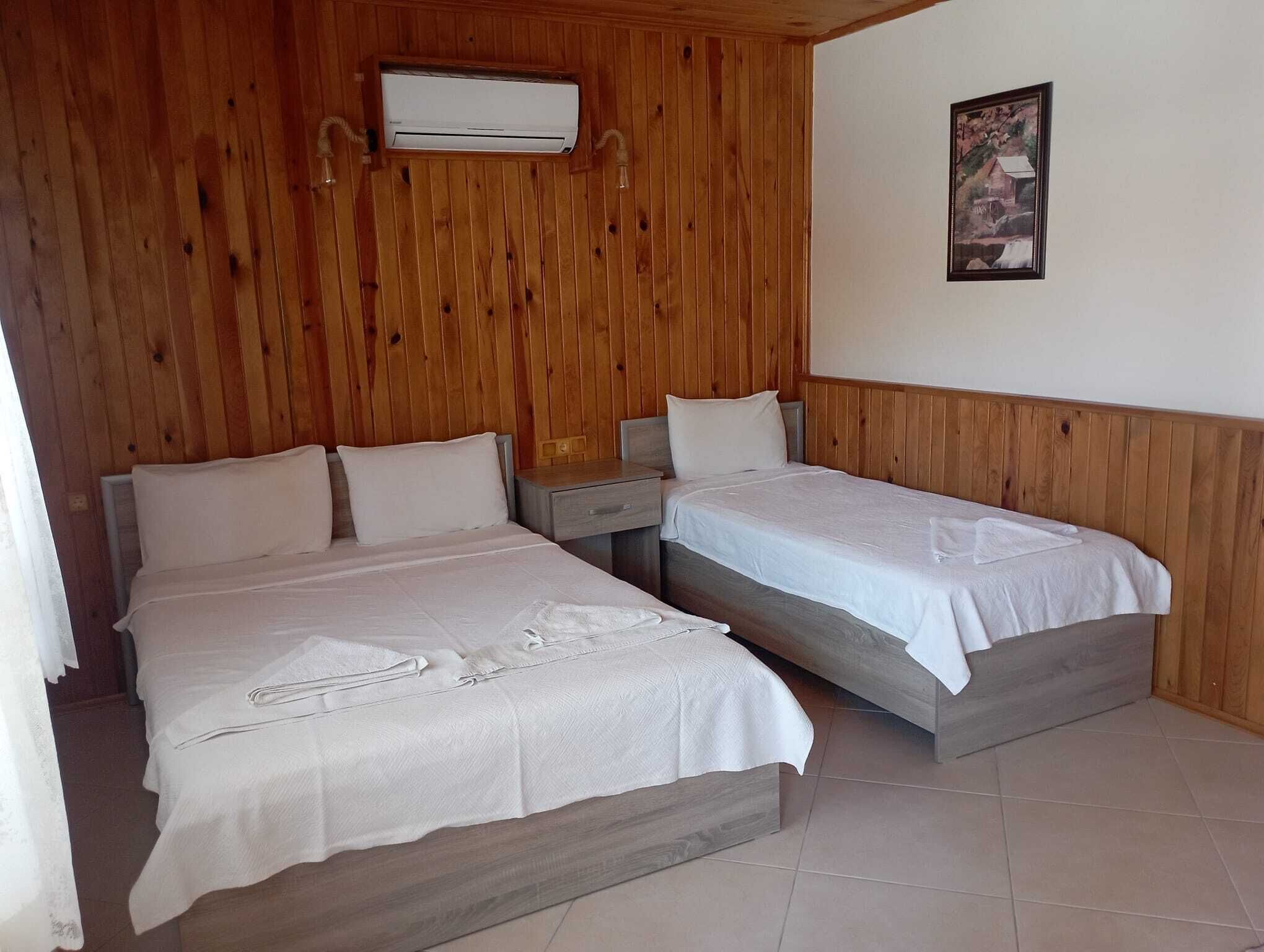A room with two beds, wooden paneling, an air conditioning unit, a nightstand, and a framed picture on the wall.