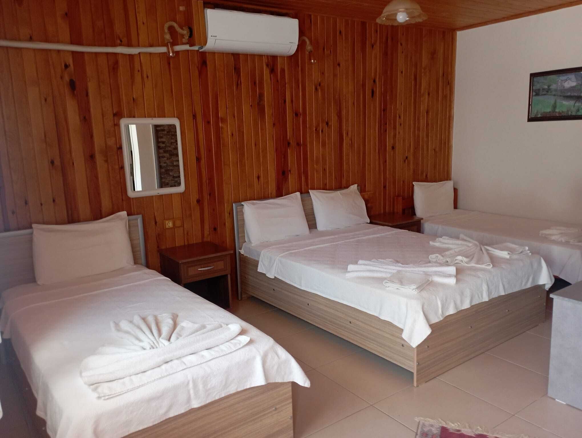 A wooden-paneled room with two beds, a nightstand, and a wall-mounted air conditioner.