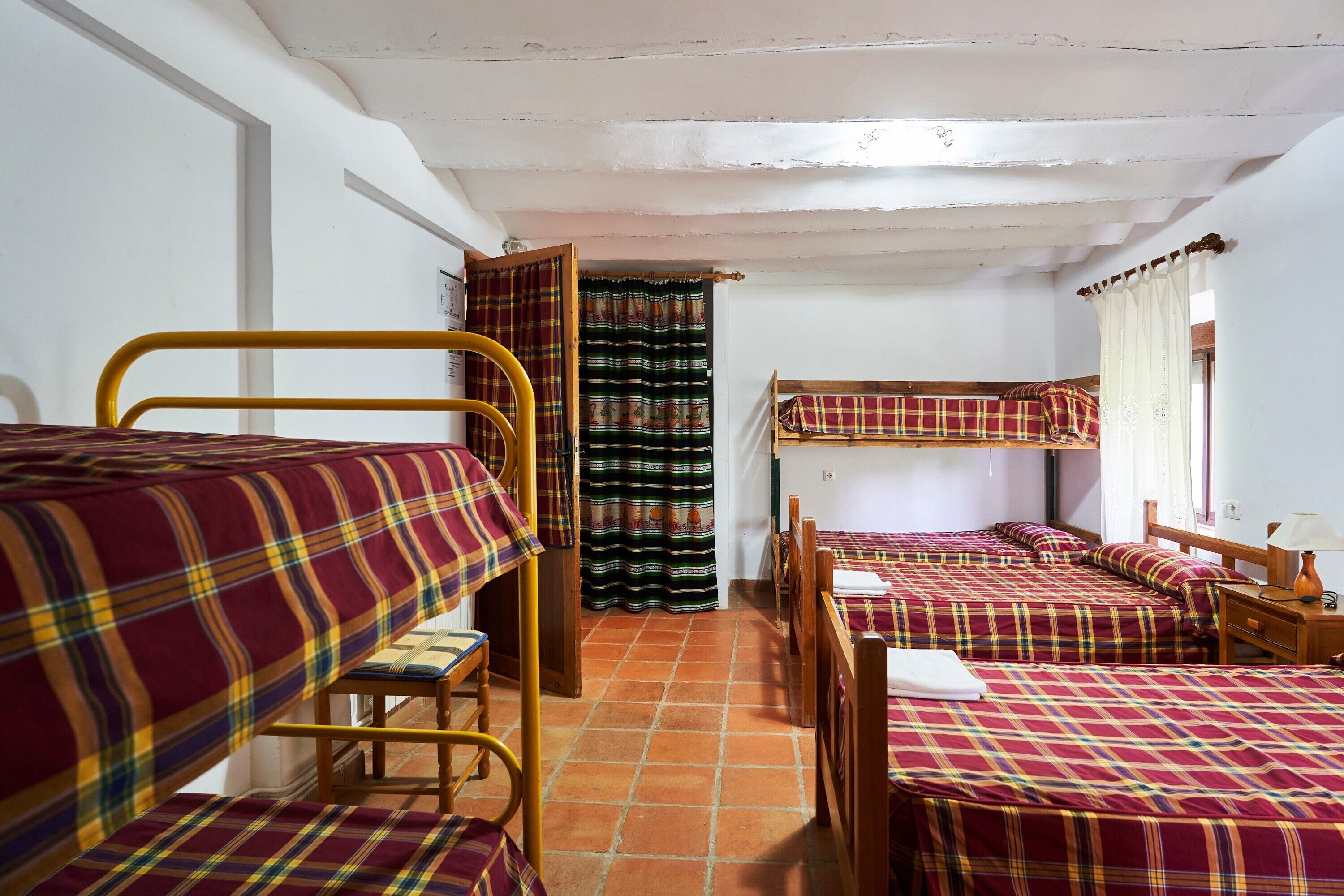 Ein Schlafsaalzimmer mit Etagenbetten, einem Holztisch, einem Stuhl und einem Fenster mit Vorhängen.