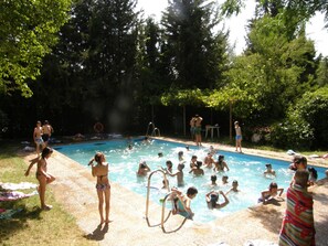 Una piscina rodeada de árboles, con gente nadando y conversando cerca.