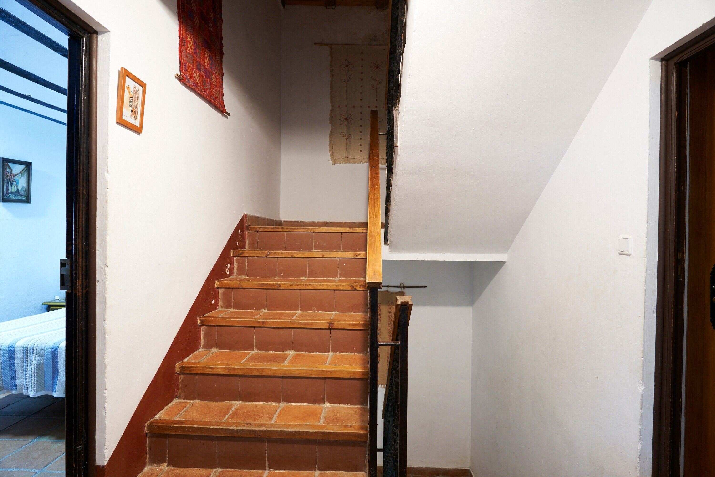 A staircase with wooden steps and a handrail, leading to a room with a bed and a window.