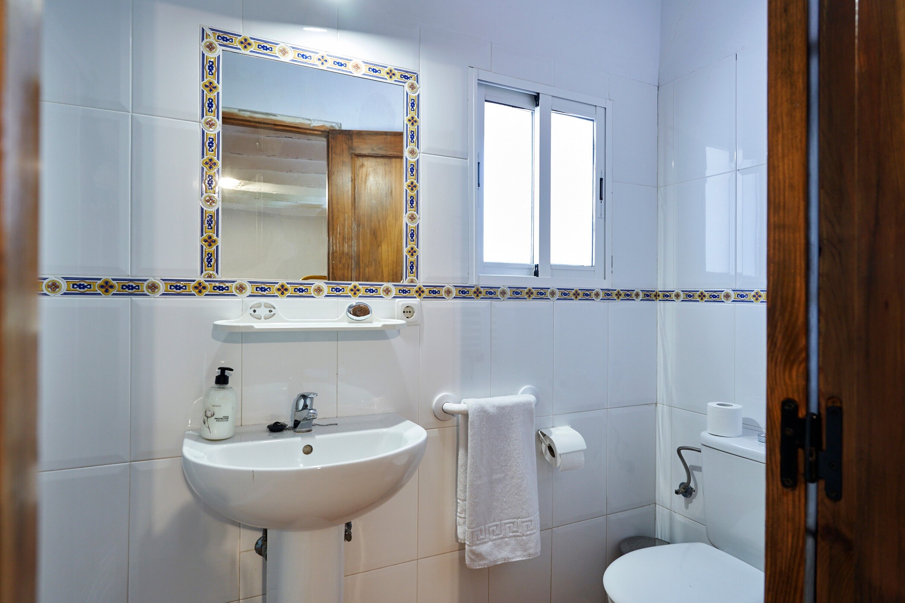 Une salle de bain équipée d’un lavabo, d’un miroir, de toilettes et d’une fenêtre.