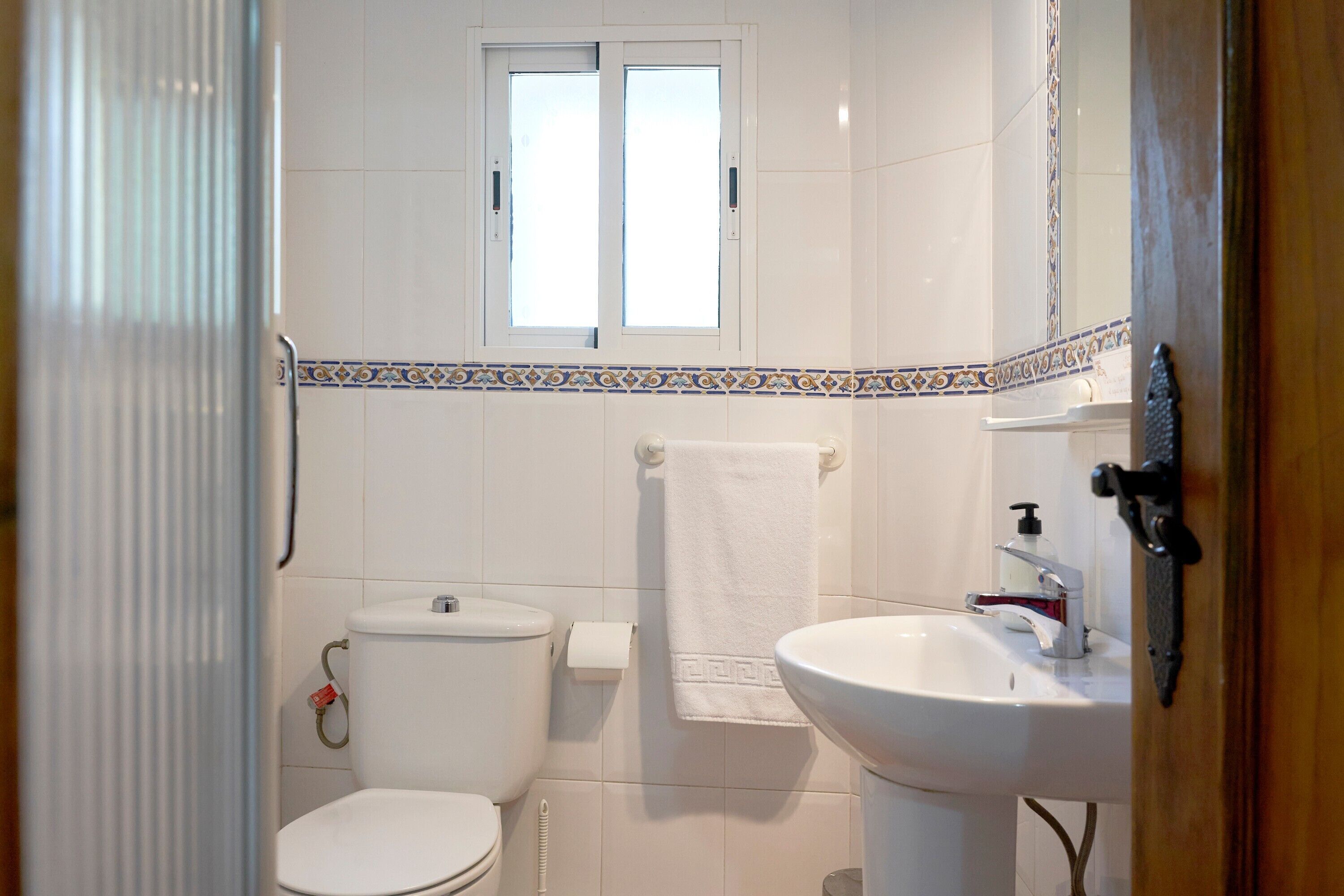 A bathroom with a toilet, sink, window, and decorative tile border.