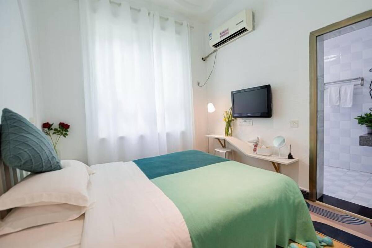 A hotel room with a bed, a desk with a computer, a television, and a shower area.
