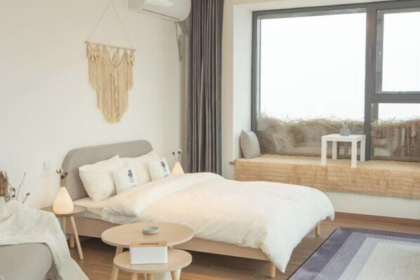 A modern bedroom with a bed, bedside table, lamp, and a view of the outdoors through a large window. - Compass B&B(Zhangjiajie Tianmenshan Ropeway Store) (Zhangjiajie)