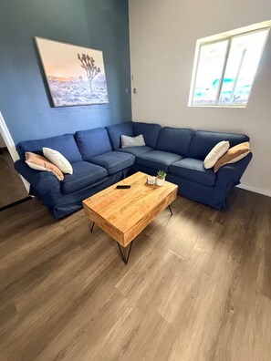 Ein Wohnzimmer mit einem blauen Ecksofa, einem Holztisch und einem Bild an der Wand.