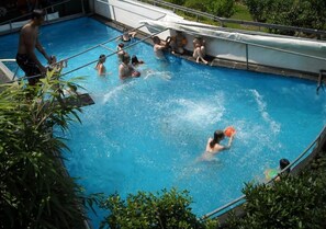 Una piscina amb persones nedant, una escala i una zona coberta.