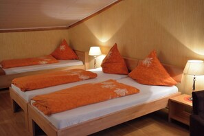 Habitación de hotel con dos camas, cada una con ropa de cama y almohadas anaranjadas, cabeceros de madera y lámparas de noche.