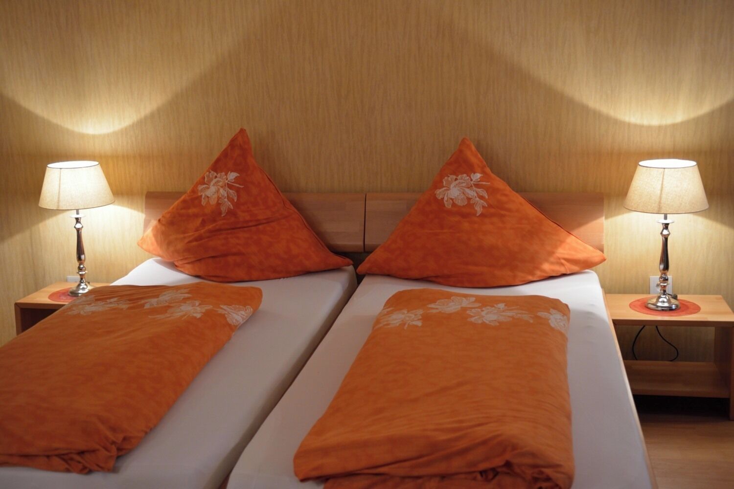 A double bed with two nightstands, each with a lamp, and matching orange pillows.