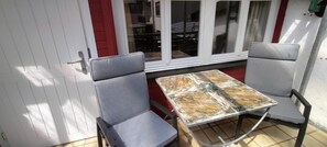 Un patio con dos sillas grises acolchadas y una mesa con superficie de vidrio.