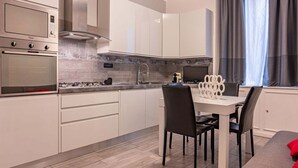 Uma cozinha moderna com armários brancos, eletrodomésticos de aço inoxidável e um espaço de refeições com mesa e cadeiras.