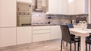 Uma cozinha moderna com armários brancos, forno embutido, fogão a gás e uma área de jantar com mesa e cadeiras brancas.