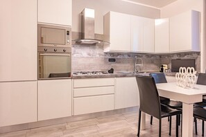 Eine moderne Küche mit weißen Schränken, einem eingebauten Backofen, einem Gasherd und einem Essbereich mit weißem Tisch und Stühlen.