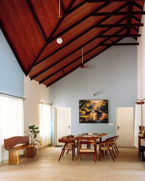 Un comedor con techo alto, vigas de madera, una mesa dispuesta para cuatro personas y un cuadro en la pared.