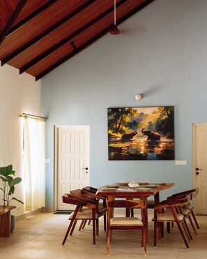 Un coin repas avec une table et des chaises en bois, un tableau au mur et un plafond avec des poutres apparentes.
