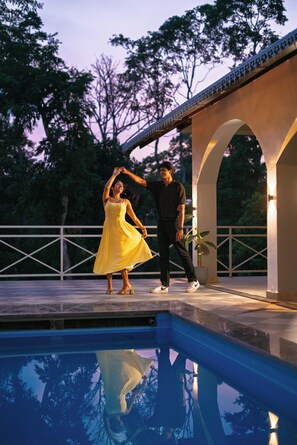 Una pareja bailando junto a una piscina, con un puente al fondo.