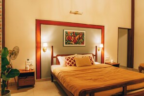 Habitación de hotel con cama de madera, dos lámparas de noche, una mesita de noche, una planta en maceta y un cuadro en la pared.