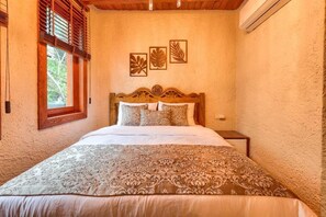Une chambre à coucher avec une tête de lit en bois, un lit avec une literie à motifs, une table de chevet et des œuvres d’art murales.