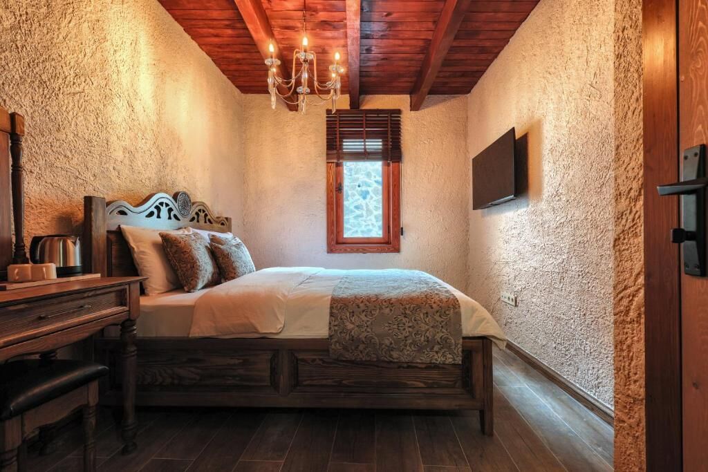 A bedroom with a bed, wooden furniture, a chandelier, a window, and a television mounted on the wall.
