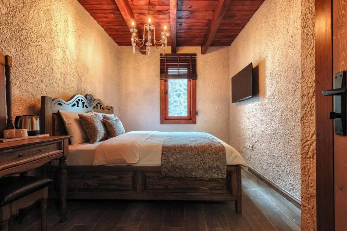 A bedroom with a bed, wooden furniture, a chandelier, a window, and a television mounted on the wall.