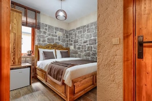 A bedroom with a stone wall, wooden bed frame, and a small kitchenette. - KALE KONAK 17 (Eceabat)