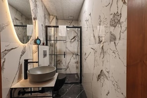 Ein Badezimmer mit einem großen Waschbecken, einer Duschkabine aus Glas und Marmorwänden.