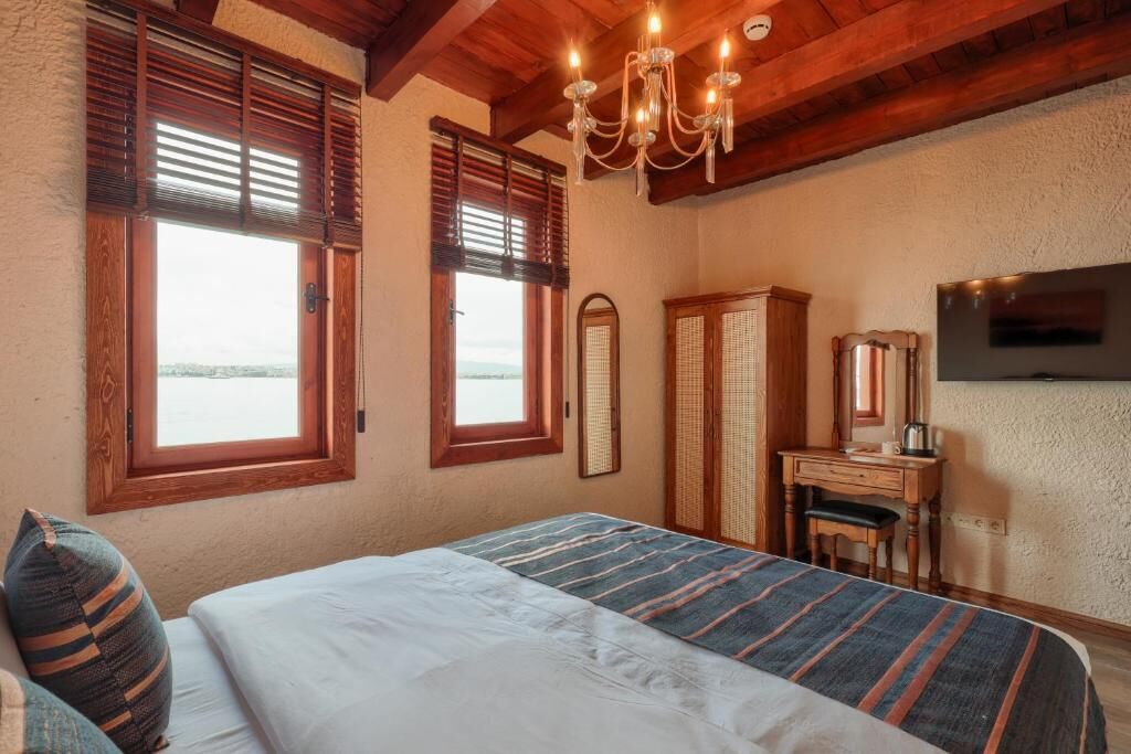 A bedroom with a bed, wooden shutters, a desk, a chair, a television, and a chandelier.