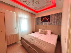 Quarto com cama, mesa de cabeceira, obra de arte na parede e luminária vermelha no teto.