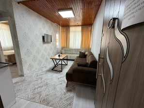 Una habitación con un sofá, una mesa de centro, un televisor montado en la pared y una alfombra estampada.