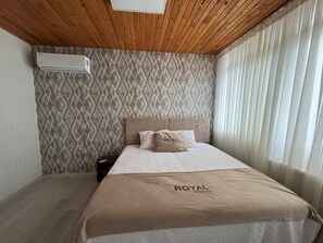 Quarto de hotel com cama, cabeceira, mesa de cabeceira, ar condicionado e janela com cortinas.