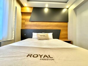 A hotel room with a bed, a headboard, and a nightstand. - ROYAL PANSİYON (Gaziantep)