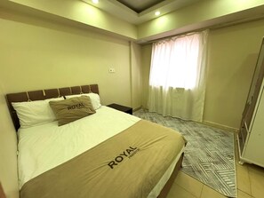 Quarto de hotel com uma cama, uma janela com cortinas, um tapete estampado e um guarda-roupa.