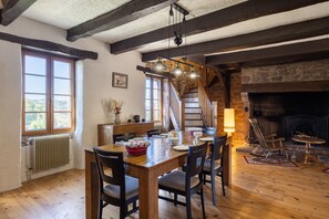 Un comedor con mesa de madera, sillas, chimenea y una escalera que sube a un nivel superior.