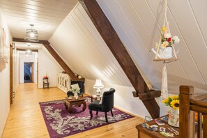 Un cuarto estilo loft con vigas de madera, un sillón negro, una mesa de madera y una lámpara colgante de macramé.