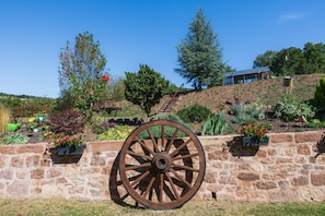 A stone wall with a large wooden wheel, surrounded by a variety of colorful flowers and plants.